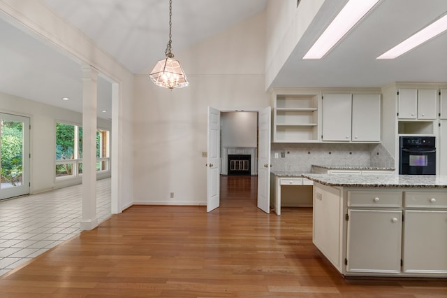 kitchen with black oven, light hardwood / wood-style flooring, pendant lighting, and lofted ceiling