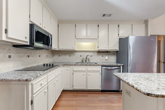 kitchen with appliances with stainless steel finishes, tasteful backsplash, sink, white cabinets, and light hardwood / wood-style floors