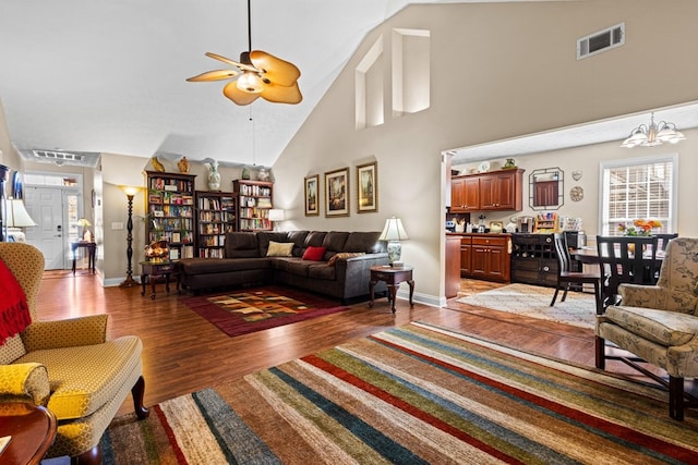 living room featuring visible vents, a high ceiling, light wood-type flooring, baseboards, and ceiling fan with notable chandelier