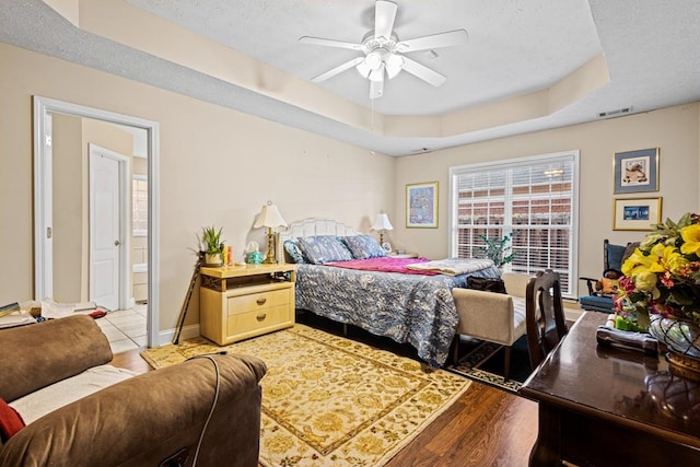 bedroom featuring a raised ceiling, visible vents, light wood-style floors, connected bathroom, and a textured ceiling