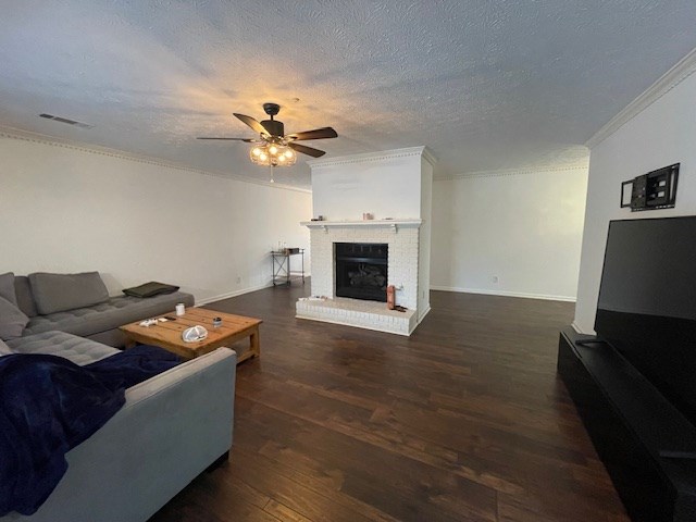 living area with visible vents, a brick fireplace, ornamental molding, wood finished floors, and a ceiling fan