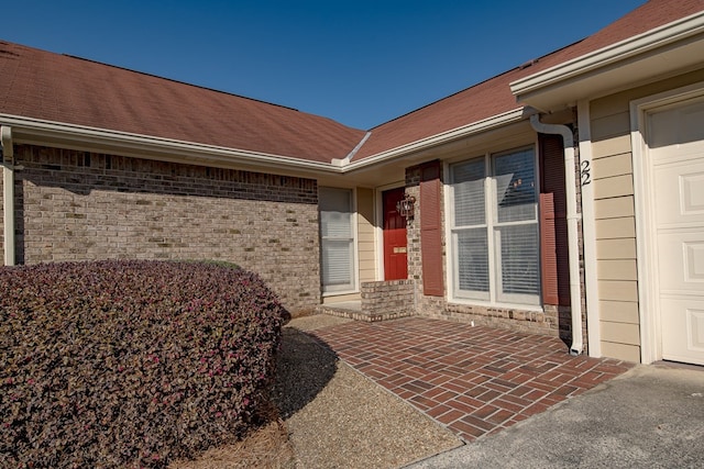 doorway to property featuring brick siding, roof with shingles, and an attached garage