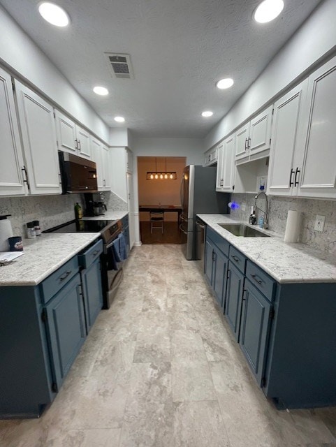 kitchen with visible vents, blue cabinetry, a sink, light countertops, and backsplash