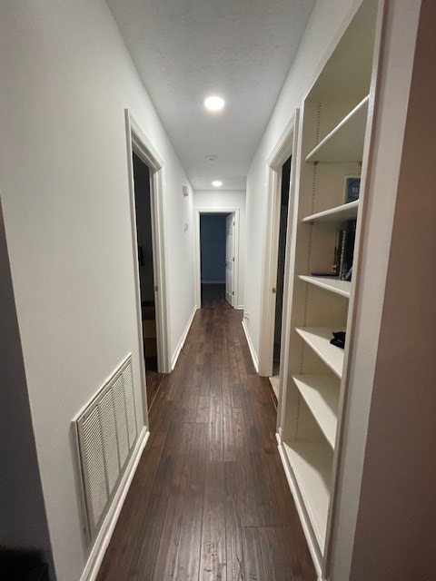 hall with baseboards, visible vents, dark wood-style flooring, and a textured ceiling