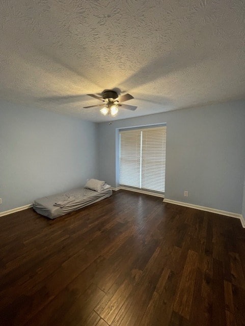 unfurnished bedroom with a textured ceiling, baseboards, dark wood-type flooring, and a ceiling fan