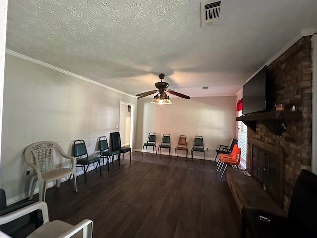 sitting room with dark wood finished floors, visible vents, a ceiling fan, a brick fireplace, and a textured ceiling