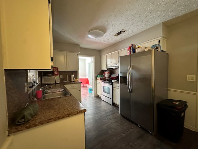 kitchen featuring dark countertops, appliances with stainless steel finishes, dark wood-type flooring, under cabinet range hood, and a sink