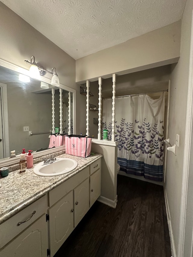 bathroom with baseboards, vanity, a textured ceiling, and wood finished floors