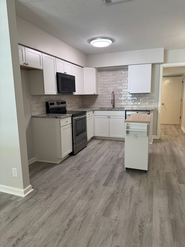1508 Emerson Ave, Columbus, GA 31907 - kitchen featuring black microwave, stainless steel range with electric cooktop, tasteful backsplash, light wood-style floors, and white cabinets