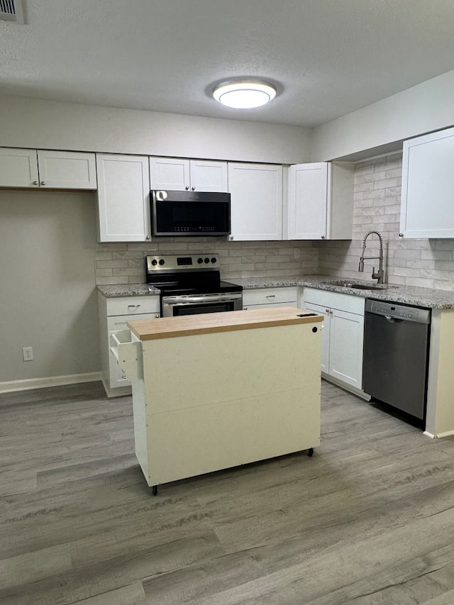 1508 Emerson Ave, Columbus, GA 31907 - kitchen featuring appliances with stainless steel finishes, backsplash, white cabinetry, light wood-style flooring, and a textured ceiling