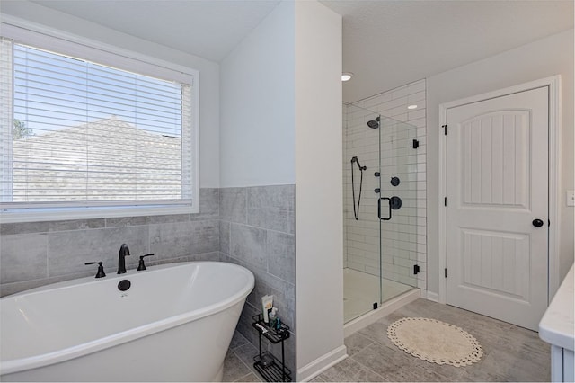 bathroom with tile patterned floors, a soaking tub, tile walls, and a stall shower