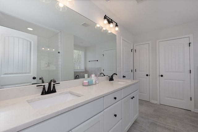 bathroom with a tile shower, visible vents, double vanity, and a sink