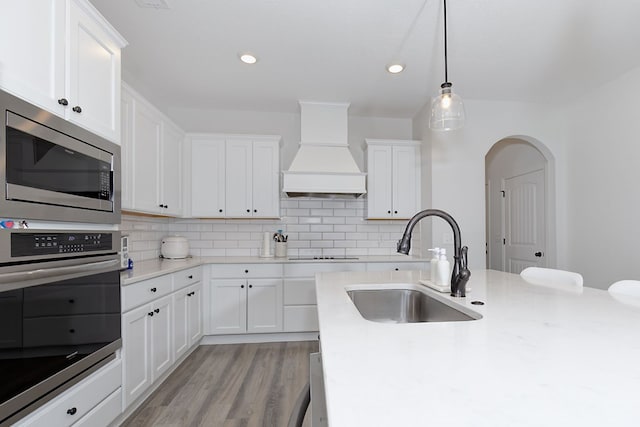 kitchen with premium range hood, arched walkways, a sink, appliances with stainless steel finishes, and tasteful backsplash