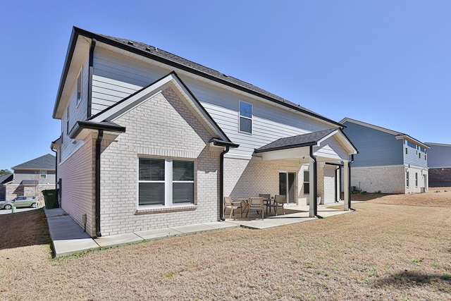 rear view of property with a patio, brick siding, and a lawn