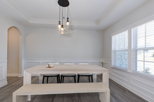 dining area with a tray ceiling, arched walkways, and dark wood-style flooring