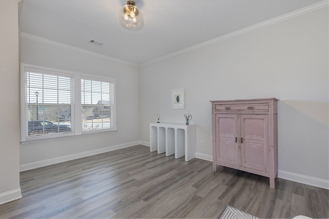 empty room featuring visible vents, light wood-type flooring, crown molding, and baseboards