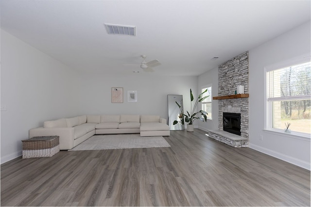 unfurnished living room featuring wood finished floors, baseboards, visible vents, a ceiling fan, and a stone fireplace