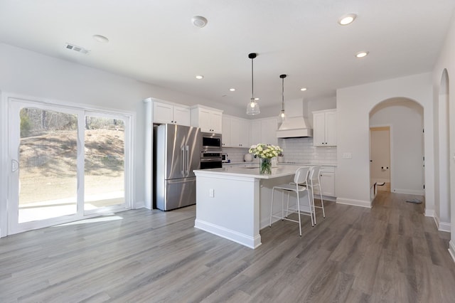 kitchen featuring visible vents, custom exhaust hood, arched walkways, appliances with stainless steel finishes, and backsplash