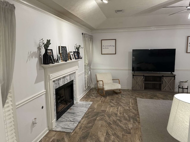 living room featuring ceiling fan, ornamental molding, a textured ceiling, a tiled fireplace, and a raised ceiling