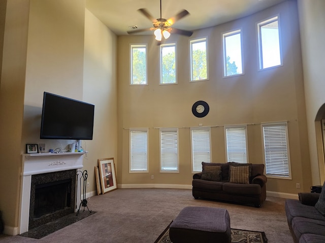 carpeted living room featuring visible vents, a high ceiling, a high end fireplace, ceiling fan, and baseboards