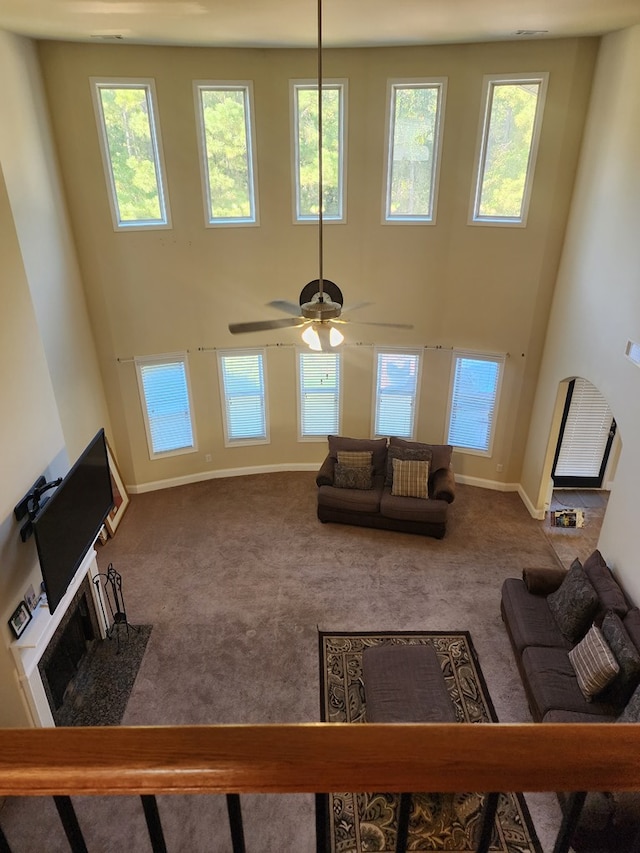 carpeted living area featuring a towering ceiling, a fireplace with flush hearth, baseboards, and ceiling fan