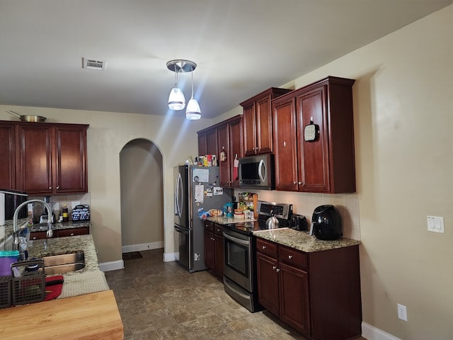 kitchen with arched walkways, a sink, appliances with stainless steel finishes, backsplash, and reddish brown cabinets