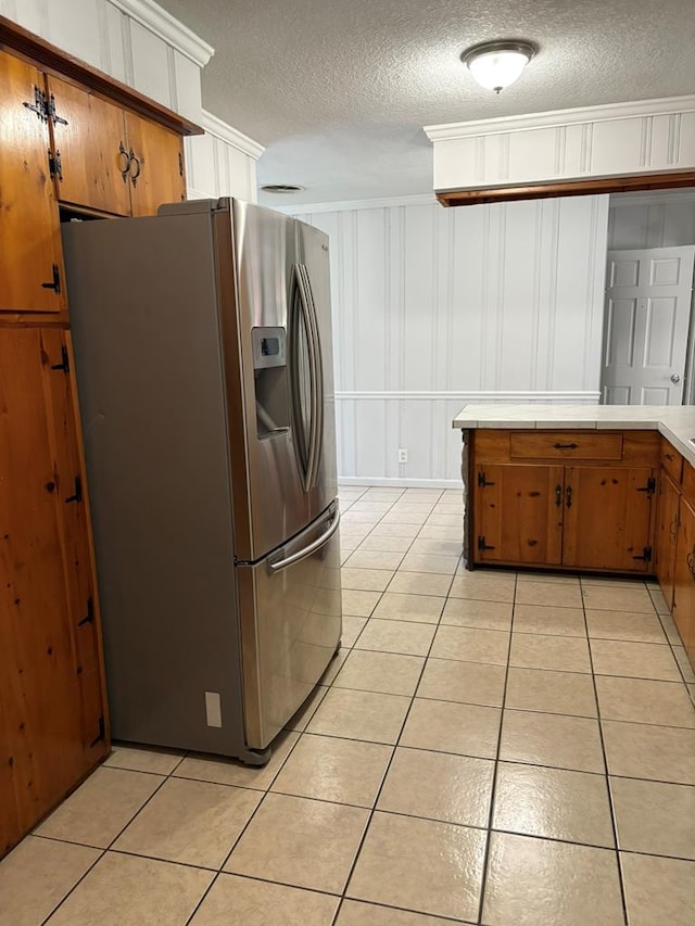 1403 Forest Dr, Columbus, GA 31907 - kitchen featuring stainless steel fridge, light tile patterned floors, a textured ceiling, brown cabinetry, and ornamental molding