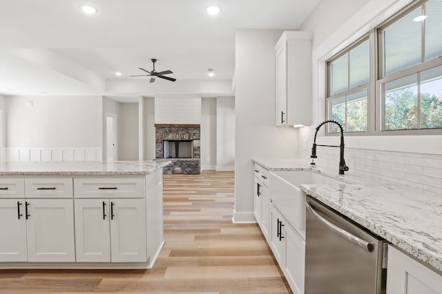 kitchen with white cabinets, light hardwood / wood-style flooring, stainless steel dishwasher, light stone countertops, and a fireplace