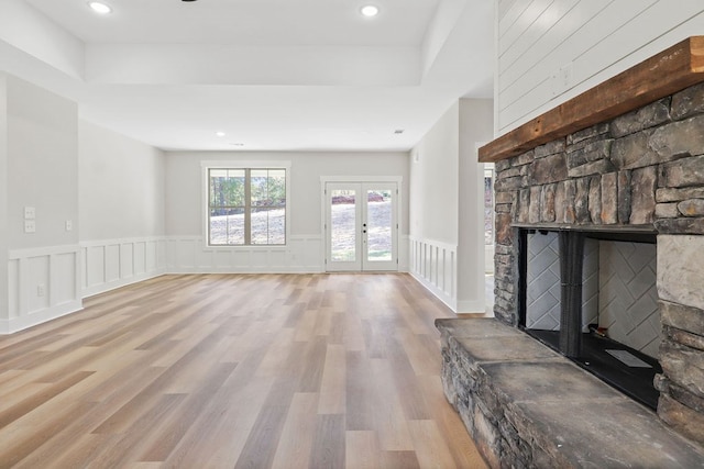 unfurnished living room with a stone fireplace, french doors, and light hardwood / wood-style floors