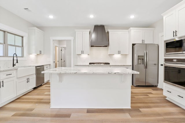 kitchen with stainless steel appliances, a kitchen island, white cabinetry, and wall chimney exhaust hood