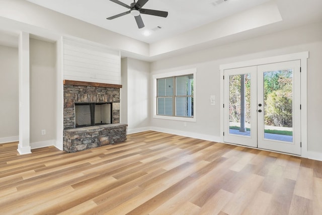 unfurnished living room with ceiling fan, a raised ceiling, light wood-type flooring, and a fireplace