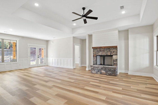 unfurnished living room featuring a fireplace, french doors, light hardwood / wood-style flooring, and ceiling fan