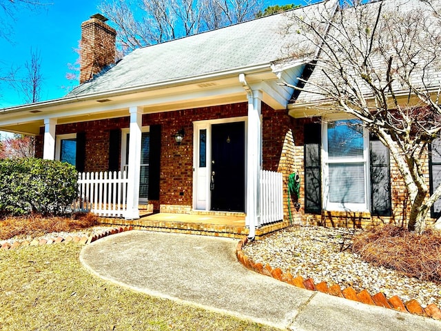 doorway to property featuring covered porch, a chimney, and brick siding