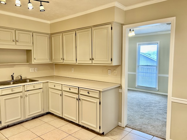 kitchen with light tile patterned floors, light colored carpet, ornamental molding, light countertops, and a sink