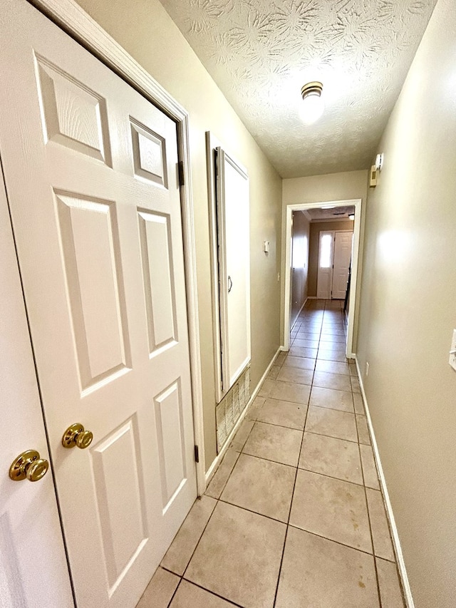 hallway with light tile patterned floors, a textured ceiling, and baseboards