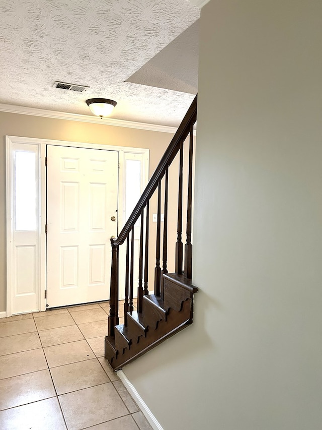 foyer entrance with light tile patterned floors, visible vents, stairway, ornamental molding, and a textured ceiling