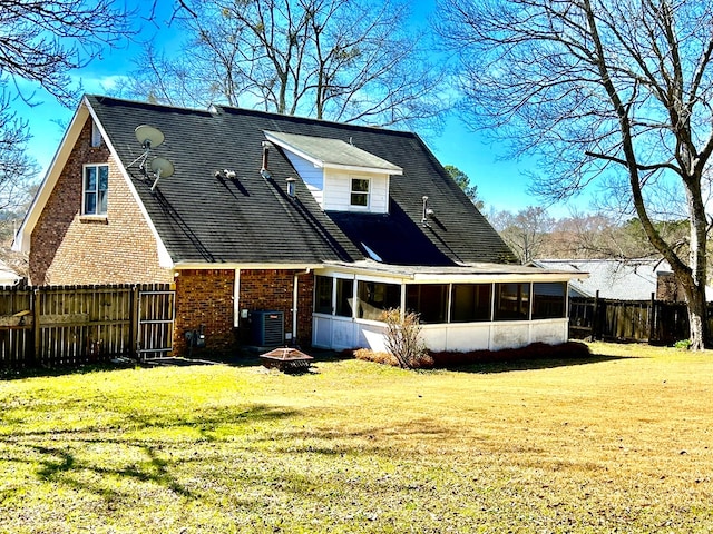 rear view of property featuring brick siding, a lawn, an outdoor fire pit, a sunroom, and fence