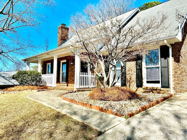 doorway to property with covered porch, a chimney, and brick siding