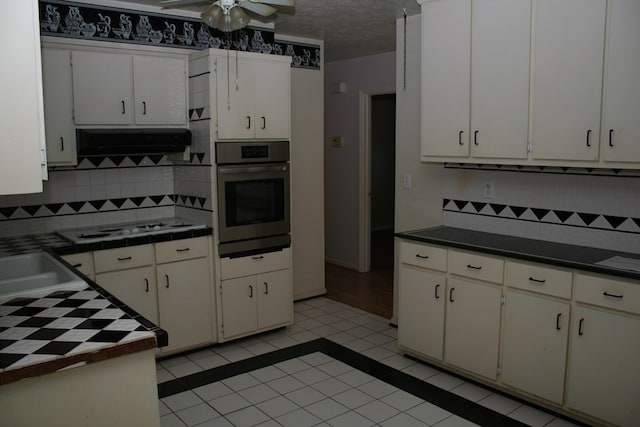 kitchen featuring white cabinets, oven, backsplash, and a textured ceiling