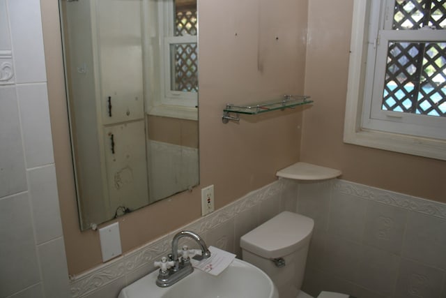 bathroom featuring toilet, tile walls, and sink