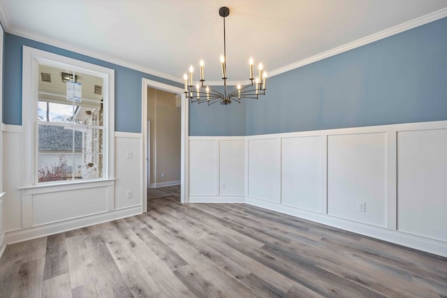 unfurnished dining area with a wainscoted wall, a decorative wall, ornamental molding, wood finished floors, and a chandelier