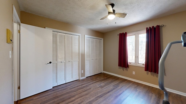 unfurnished bedroom with baseboards, multiple closets, a textured ceiling, and wood finished floors