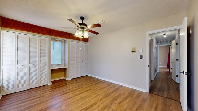 unfurnished bedroom with light wood-style floors, baseboards, two closets, and a ceiling fan