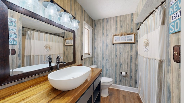 bathroom with toilet, wood finished floors, wallpapered walls, baseboards, and vanity