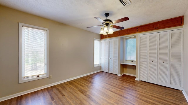 unfurnished bedroom featuring visible vents, multiple windows, wood finished floors, and built in desk