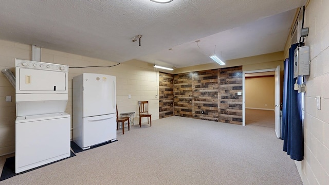 finished below grade area with a textured ceiling, freestanding refrigerator, carpet, concrete block wall, and stacked washer / drying machine