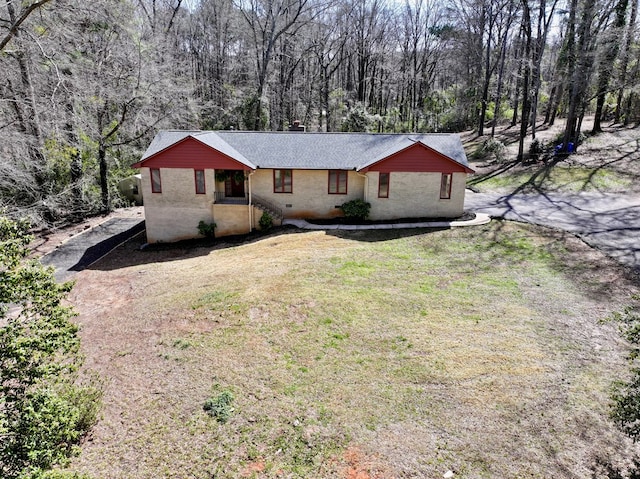 single story home featuring a forest view, roof with shingles, a front lawn, crawl space, and brick siding