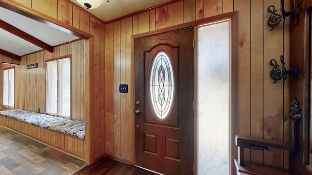 foyer entrance featuring dark wood-type flooring, beamed ceiling, wood walls, and ornamental molding