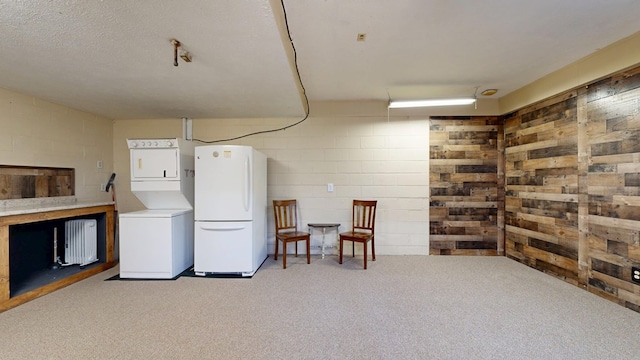 laundry room with concrete block wall, carpet floors, laundry area, radiator heating unit, and stacked washer and clothes dryer