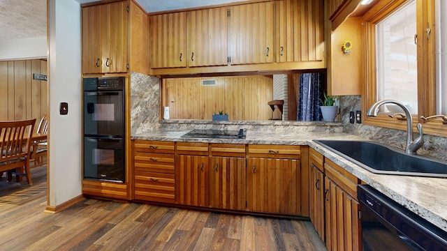 kitchen with black appliances, a sink, dark wood finished floors, brown cabinetry, and light countertops